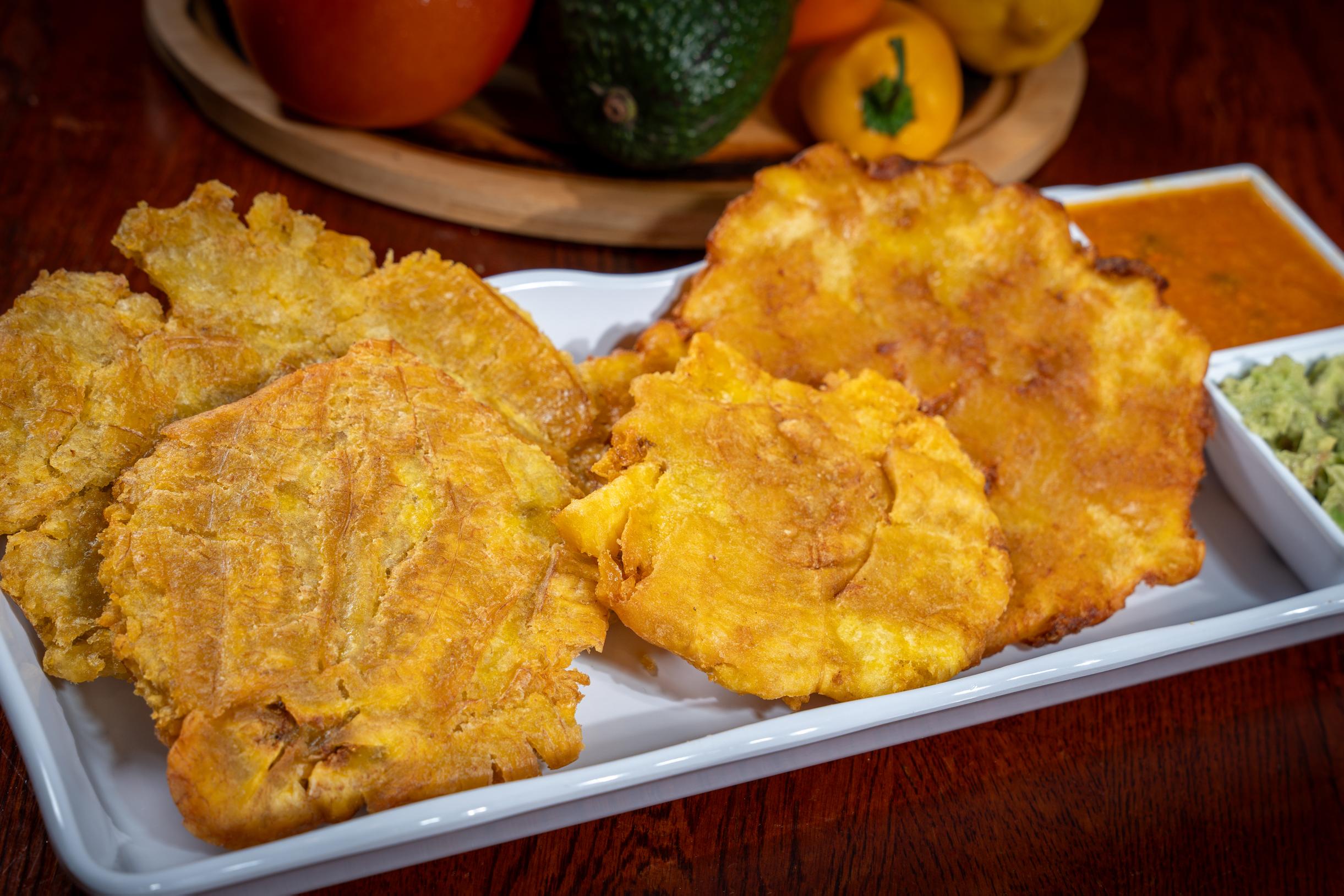 Crispy double-fried green plantains served with fresh guacamole and tomato-onion hogao sauce in Davie, FL.